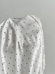 Close-up detail shot of white fabric featuring black polka dots and delicate white lace trim.