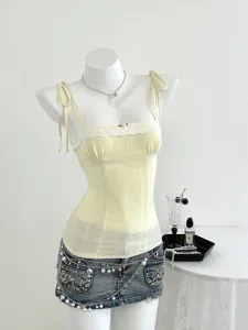 Top a corsetto giallo con pizzo e gonna di jeans con perle, dettaglio estetico chic.
