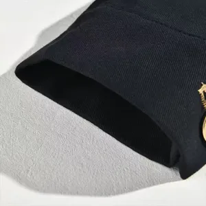 Detalle de puno de chaqueta casual de hombre con boton metalico dorado, tela negra.