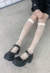 Details of sheer white floral patterned mid-calf socks paired with black Mary Jane shoes.