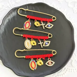 Closeup of red woven rhinestone brooch pins featuring evil eye, cross and religious charm details.