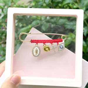 Close-up detail of the gold alloy safety pin with red braided rope and multi-charms pendant.