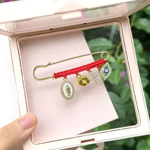 Detail view of red rope woven rhinestone brooch featuring evil eye, cross and religious charms.