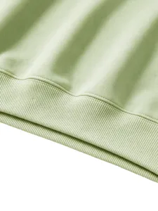 Close-up detail of the ribbed hem on a casual solid green kids sweatshirt, soft fabric texture.