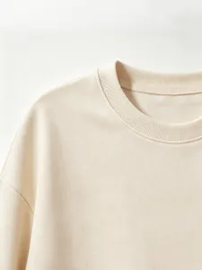 Close-up detail of soft beige crewneck sweatshirt fabric, showing fine ribbed collar texture.