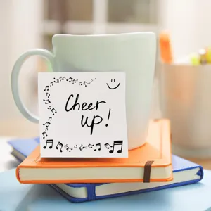 Close-up detail of a cute sticky note with musical notes and cheer up text on a desk.