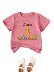 Dettaglio della maglietta rosa da neonato con nome Clara e stampa di treno con animali.