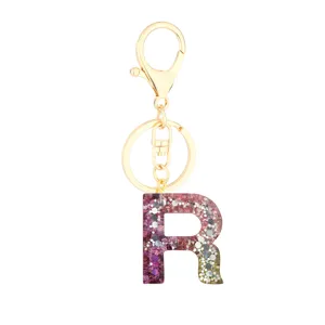 Close-up of pink glitter resin letter R pendant with gold metal keychain hardware details.