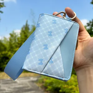 Close-up of light blue leather cardholder with wrist strap, bow pattern and metal keychain ring.