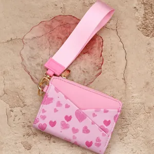 Pink leather card holder wallet with wrist strap and cute heart print pattern detail.