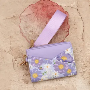 Close-up detail of a purple leather card holder wallet with floral print and wrist strap.