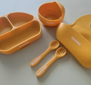 Silicone baby tableware set with divided plate, bowl, spoon, fork, and bib in yellow.