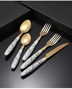 Close-up detail of luxury gold stainless steel cutlery set with black ink splash ceramic handles.