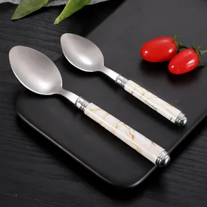 Stainless steel spoons with white marble ceramic handles set on black tray for dining table