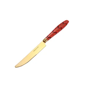 Stainless steel steak knife with gold plated blade and red chevron pattern handle for dining table.