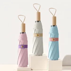 Detalle del paraguas plegable con mango de madera natural y práctico cordón para colgar.