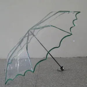 Transparent clear folding umbrella with green lace ruffle edge for rain and sun protection.
