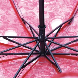 Detail shot of folding umbrella black metal ribs and red lace transparent canopy fabric.