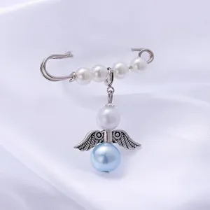 Close up detail shot of the silver safety pin brooch featuring white pearls and angel pendant.