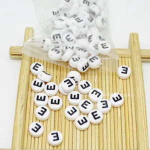 Nahaufnahme von weißen Acryl flachen runden Buchstabenperlen verstreut auf Bambustablett.