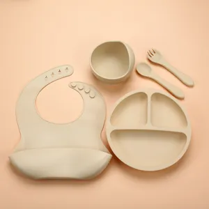 Baby silicone feeding set detail showing divided plate bowl bib spoon fork beige color.