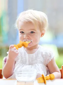 Gros plan d'un tout-petit mangeant avec un ensemble cuillère et fourchette d'apprentissage.