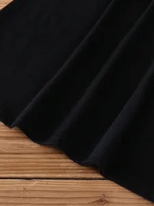 Close-up view of a solid black t-shirt showing fabric texture and fine hem stitching on a wooden surface.