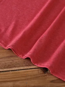 Close-up detail of soft red cotton fabric with neat stitching on wooden background surface.