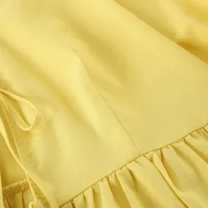 Gelbe Damenbekleidung Stoff Detail Nahaufnahme mit weicher Textur Rüsche Design und Band.