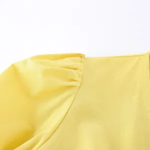 Nahaufnahme des gelben Damenoberteils mit Puffärmeln und eleganten Schulterfalten im Detail.
