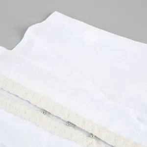 Nahaufnahme Detail eines weißen Baumwoll-Tops mit beiger Spitzenborte und Metallschließen.