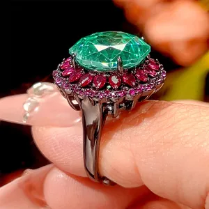 Nahaufnahme des luxuriösen Schwarzgoldrings mit ovalem grünem Hauptstein und rotem Schmuckstein.