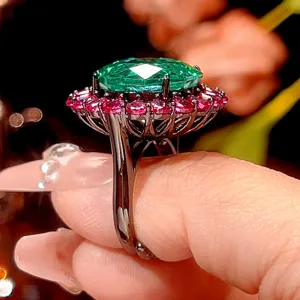 Detailed close-up of luxury black gold halo ring with large green gem and red stones.
