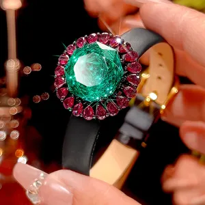 Close-up view of luxury black gold jewelry watch with sparkling green and red gemstone details.
