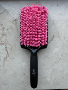 Detail view of a hair drying brush with pink absorbent chenille bristles and a black handle.