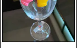 Primo piano dettaglio di calice in vetro trasparente con indicatori di vino in silicone colorato, festa.