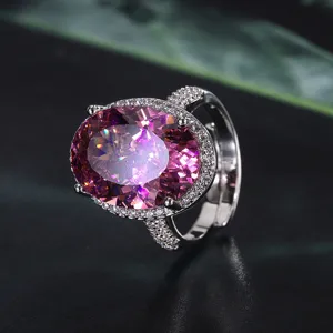 Primo piano dettagliato di un grande anello con gemma ovale rosa, alone pavé e fascia divisa lucida.