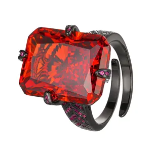 Close-up of a bold black gold ring featuring a large red radiant cut gemstone with small pavé stones.