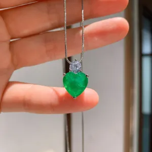 Primer plano detalle de un collar plateado con un colgante de gema verde en forma de corazón.