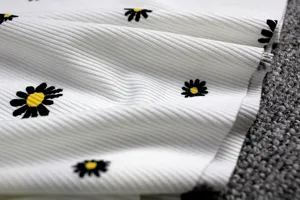 Close-up detail of white ribbed cotton fabric with black and yellow daisy print pattern.