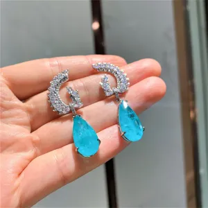 Gedetailleerde close-up van blauwe edelsteen oorbellen, zilveren maan pavé ontwerp