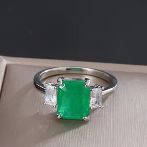 Primo piano di un anello con smeraldo verde rettangolare e pietre laterali in zircone.