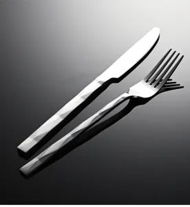 Primer plano detallado de cuchillo y tenedor de acero inoxidable con mango de diseño geométrico.