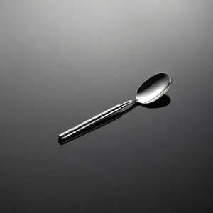 Close-up of stainless steel dessert spoon with hammered handle texture, elegant tabletop detail.