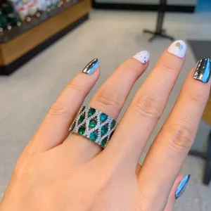 Primer plano detallado de un anillo ancho retro con piedras verdes y brillantes circonitas.
