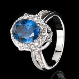 Detalle impresionante de anillo ovalado con piedra preciosa azul, circonitas y banda brillante.