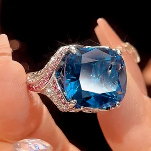 Close-up detail shot of luxury cushion cut blue gemstone ring with pink paved stones on band.