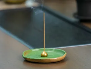 Gedetailleerde close-up van de groene keramische wierookhouder met brandend stokje.