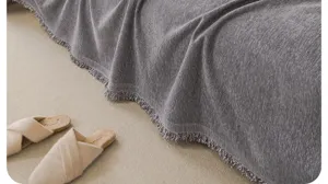 Grey chenille sofa blanket detail shot showcasing soft fabric texture and elegant fringe trim.