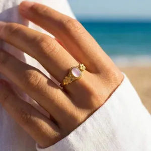 Close-up detail of the 18k gold stainless steel pink crystal floral ring on beach background.